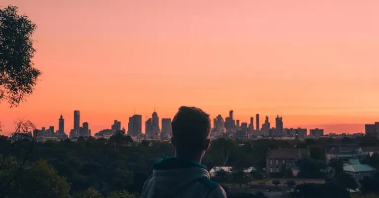 Man In Green Hoodie Looking At City Buildings During Sunset