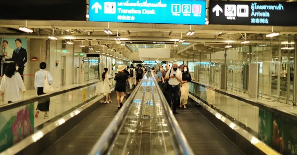 Passengers Walk On A Travelator In An Airport Arrival Area, Surrounded By Signs And Bright Lighting.