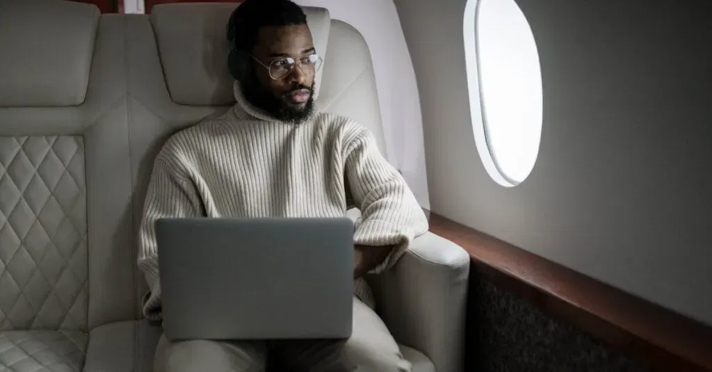A Man Wearing Headphones Uses A Laptop In A Luxurious Airplane Cabin.