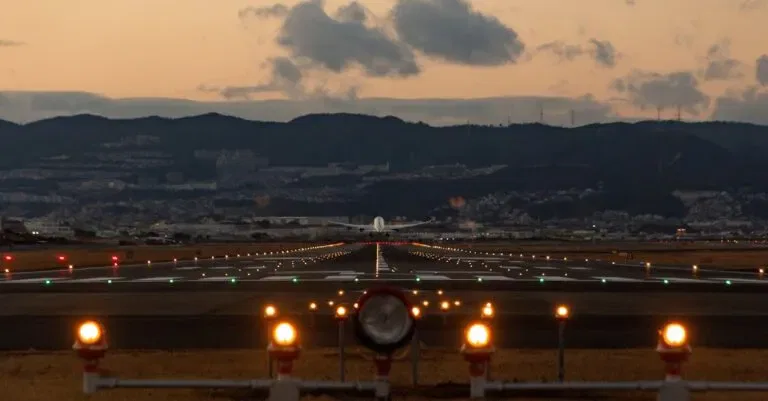Scenic View Of Airplane Landing On Osaka Runway During Dusk With City Skyline.