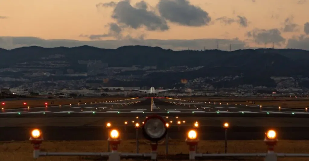 Scenic View Of Airplane Landing On Osaka Runway During Dusk With City Skyline.