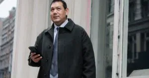 Low Angle Of Confident Adult Ethnic Male Manager In Classy Suit And Coat Standing On Street Near Building And Browsing Mobile Phone