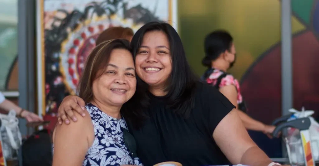 A Mother And Daughter Sharing A Joyful Embrace In A Colorful Airport Terminal.