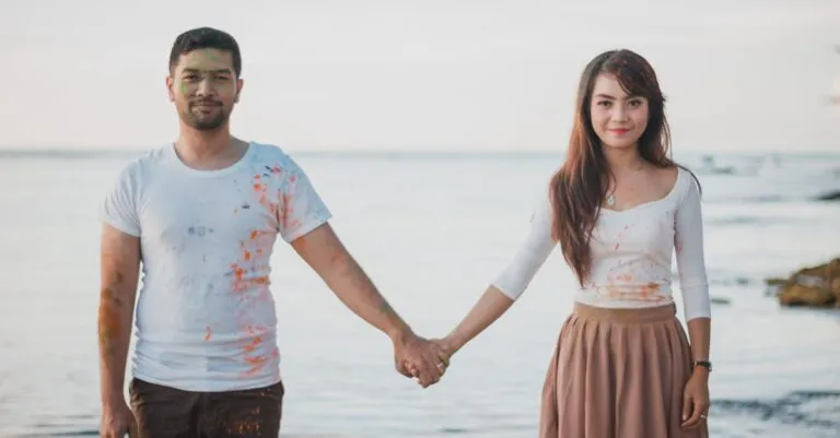 A Cheerful Couple Holding Hands By The Sea, Enjoying A Playful Day With Paint Splashes.