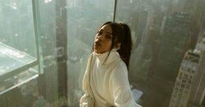 Luxury Car &Amp; Limo Services Articles &Amp; News 7 May 20, 2026 Young Woman In Cozy Sweater Posing By A Glass Wall Overlooking New York City From A Skyscraper.