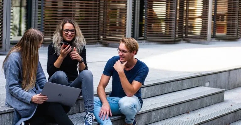 Three Young Professionals Having A Friendly Chat While Sitting On Outdoor Steps.