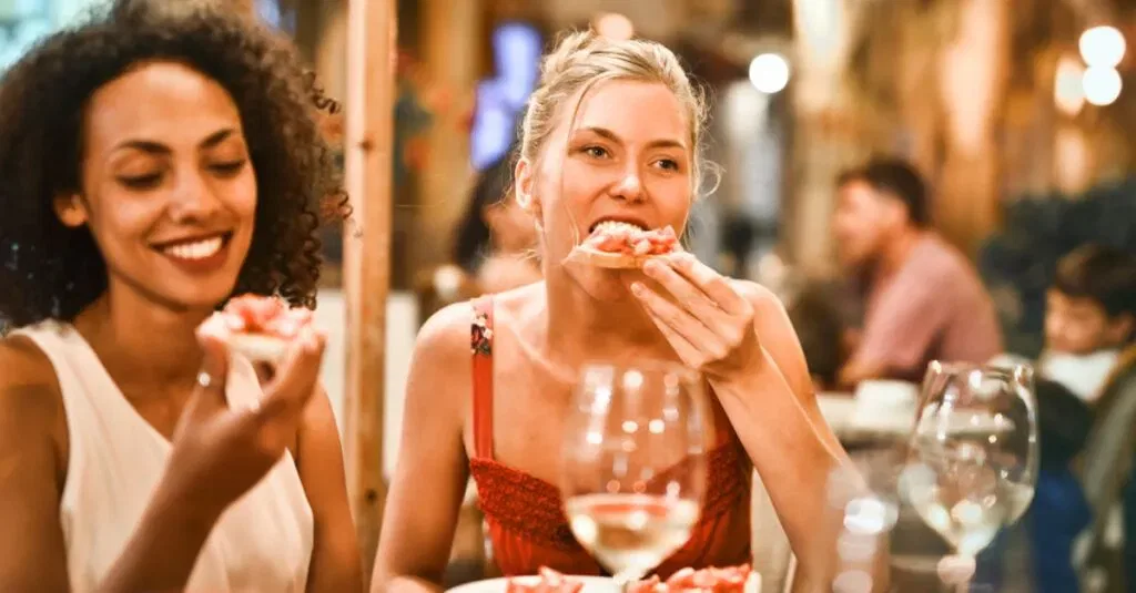 Two Women Enjoying Bruschetta And Wine At A Vibrant Outdoor Restaurant.