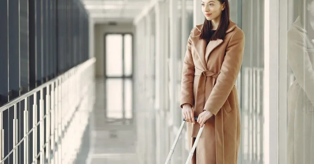 Elegant Woman In A Beige Coat With Luggage In A Contemporary Airport Corridor.