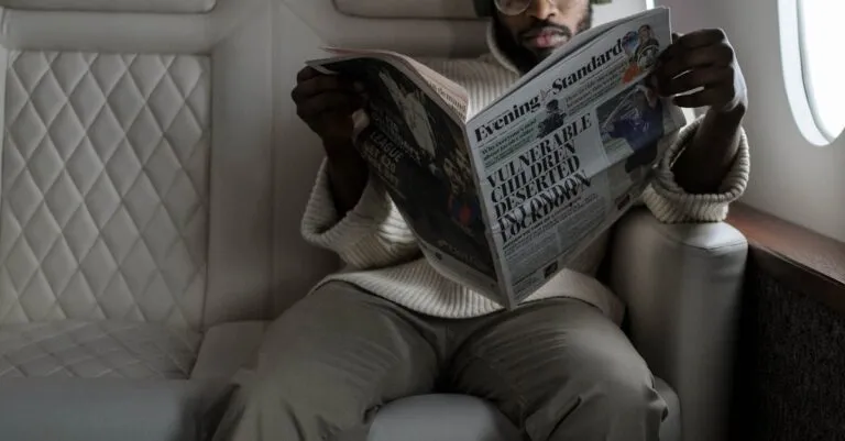 African American Man Reading Newspaper And Listening To Music In Airplane Cabin With Headphones.