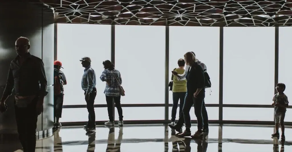 Silhouettes Of Tourists Observing The Dubai Skyline From An Indoor Observation Deck.