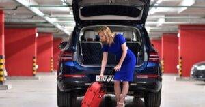 Stylish Woman In A Blue Dress Placing Luggage In Car Trunk In A Parking Garage.