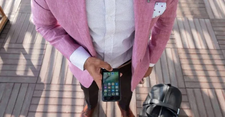 Stylish Man In A Pink Blazer Checks His Smartphone While Traveling With A Leather Bag.