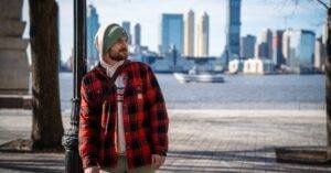 A Man In Casual Winter Attire Stands With Manhattan Skyline In The Background.