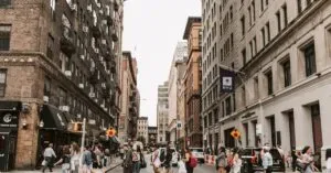 People Crossing A New York Street Lined With Historic Buildings On A Busy Day.