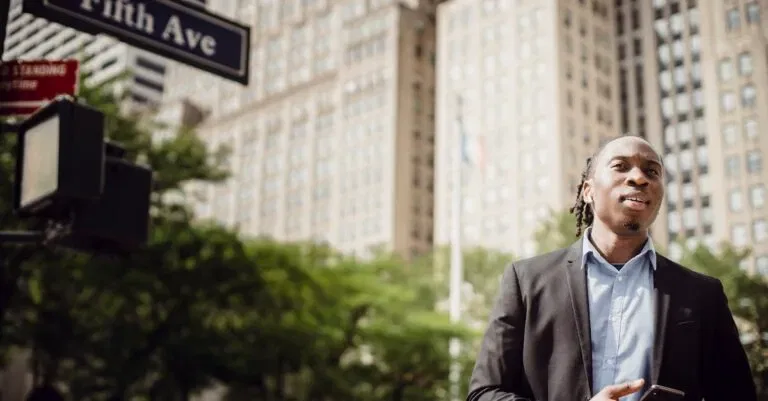 A Young Man Stands On Fifth Avenue In New York City Holding A Smartphone, Showcasing Urban Lifestyle.