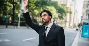 A Man In A Suit Raises His Hand To Hail A Taxi On A City Street.