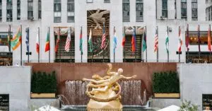 Golden Prometheus Statue Located Near Entrance Of Rockefeller Center With Flags On Street In New York City In Modern District
