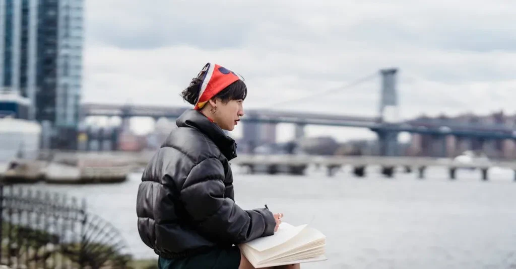 Side View Of Pensive Asian Female Taking Notes In Notebook And Looking Away While Sitting On Stone On Embankment In City In Daylight