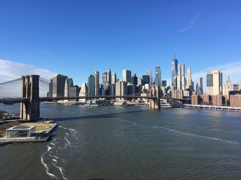 Stunning View Of The Brooklyn Bridge With Manhattan Skyline Under A Clear Blue Sky.