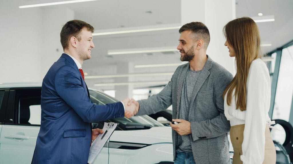Best Car Service In 10029: Your 2026 Guide To Reliable Nyc Black Car Rides From East Harlem 4 April 13, 2026 Friendly Handshake Between A Car Salesman And Customers In A Modern Car Showroom.