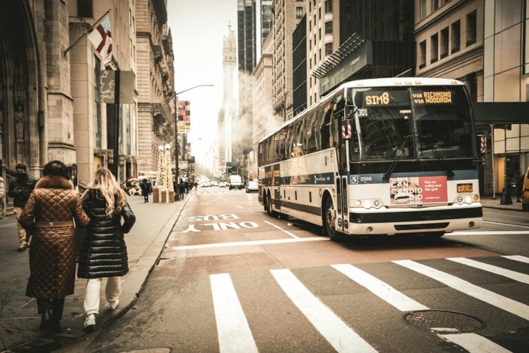 A Downtown Scene Featuring A City Bus, Pedestrians, And Urban Architecture.