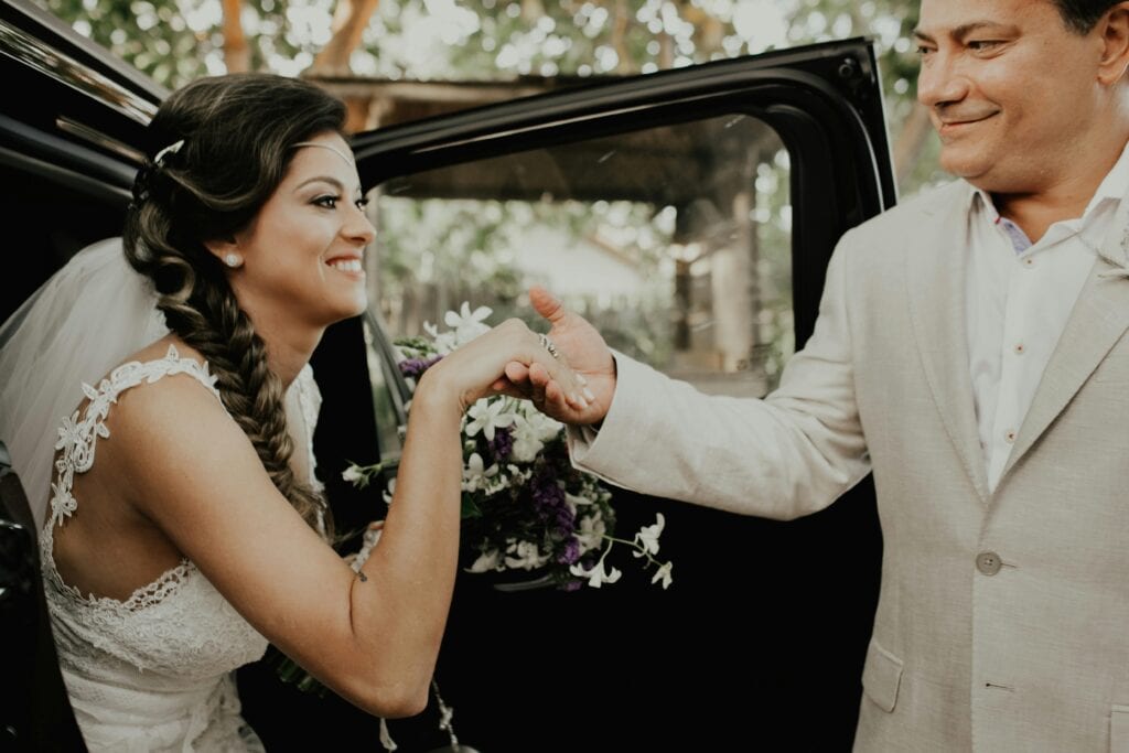 Bride Steps Out Of Car With Groom'S Assistance In A Lovely Wedding Scene.