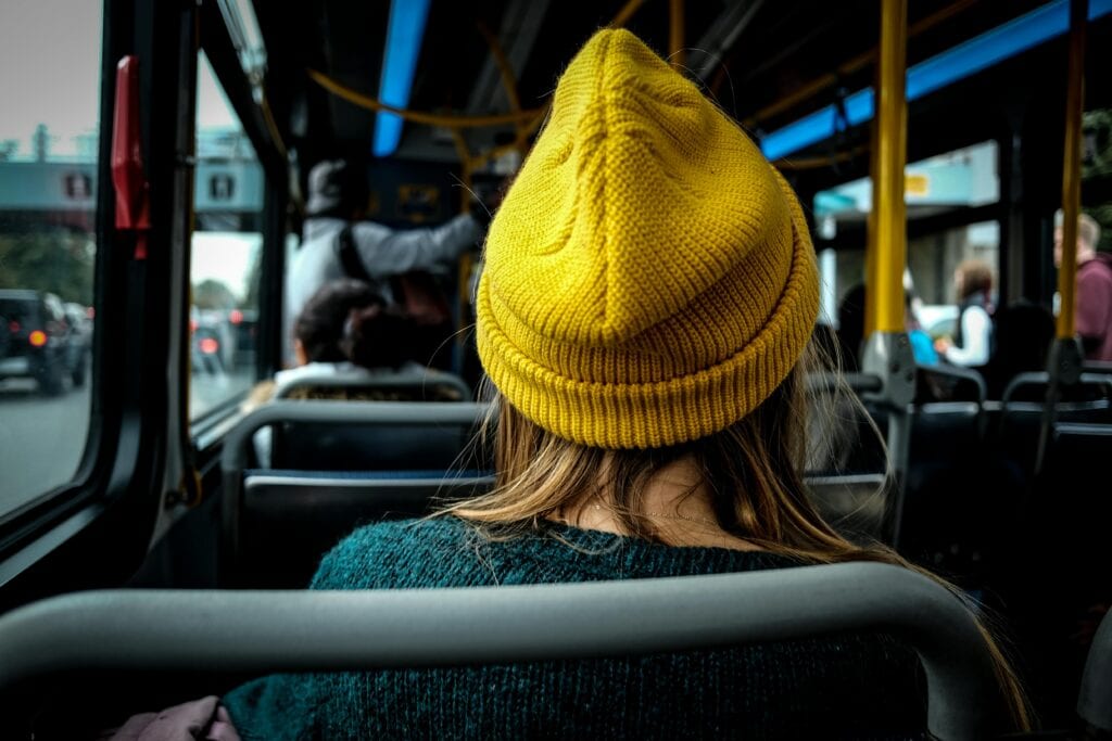 Woman In A Yellow Beanie Riding On A Public Bus, Viewed From Behind.
