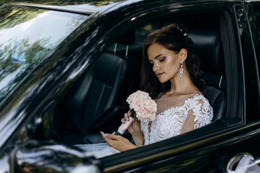 Cheap Limos Nj In 2026: Honest Truth About Getting Luxury Without Getting Fleeced 3 April 13, 2026 A Bride Wearing A Lace Wedding Dress Holds A Bouquet Sitting In A Car, Ready For Her Wedding Celebration.