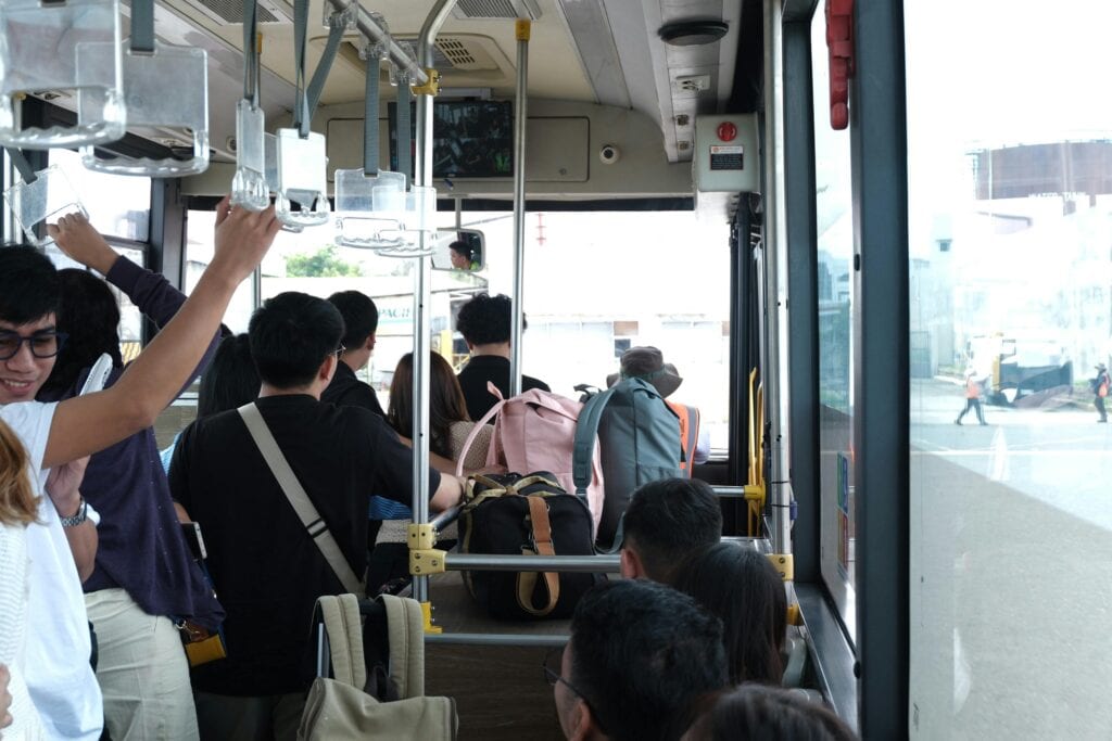 Passengers On A Bus Ride, Holding Onto Rails And Carrying Backpacks, Showcasing Urban Transportation.