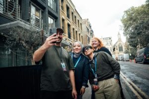 Group Of Friends Taking A Selfie On A Lively Street In London With A Church In The Background.