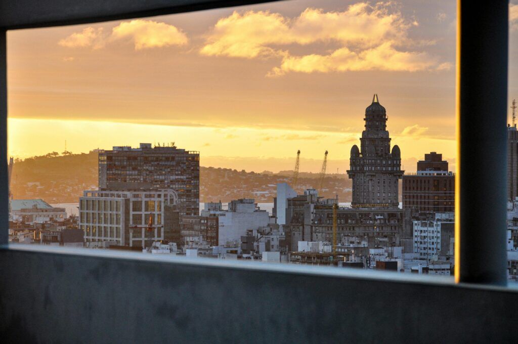 Scenic Sunset View Of Montevideo Shown Through A Window, Highlighting The Iconic Palacio Salvo.