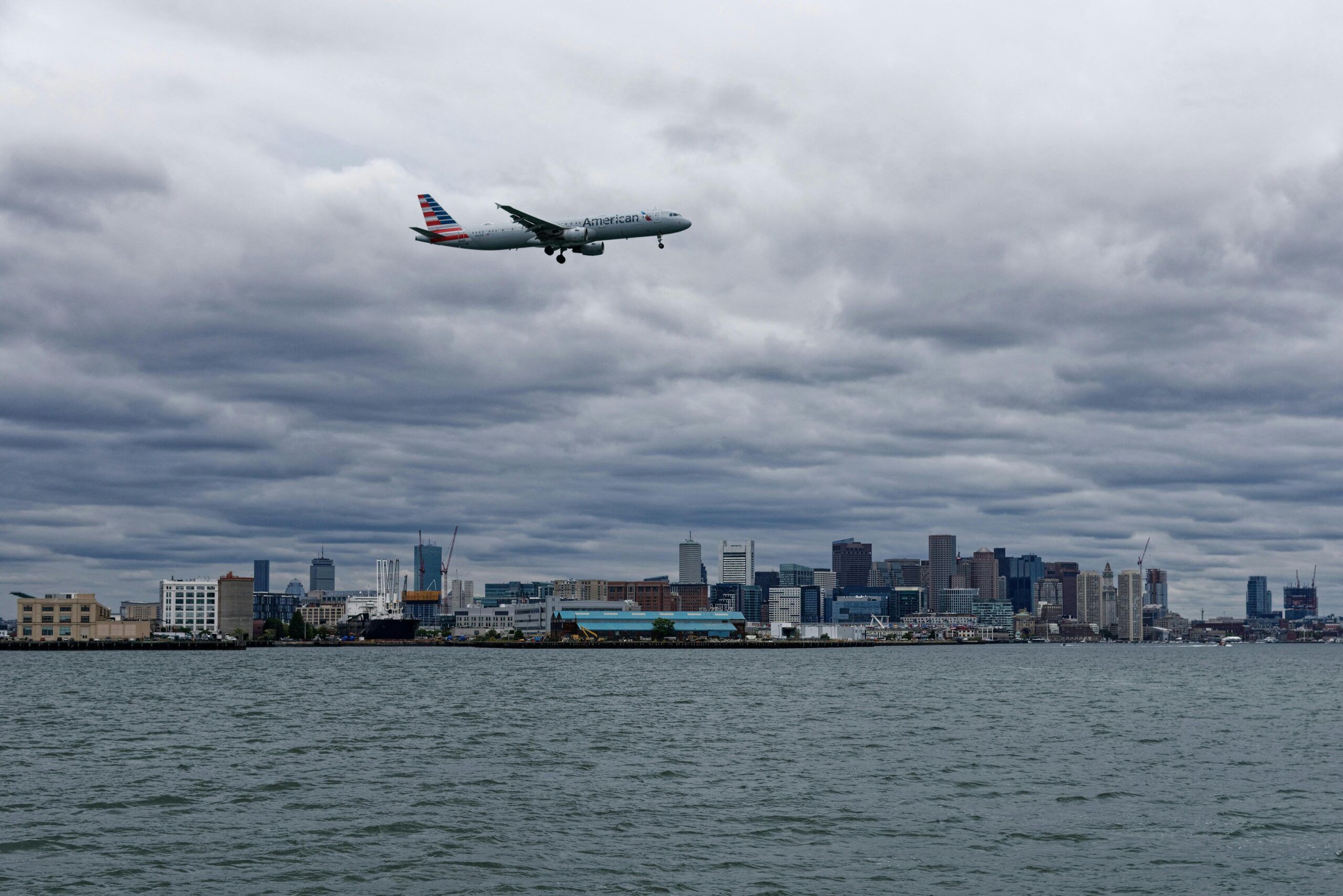 Blogs | Articles | News | Tips &Amp; Tricks | Video | Faq | Infomation 1 April 12, 2026 Passenger Plane Flying Over Water Towards Boston Skyline, Cloudy Day.