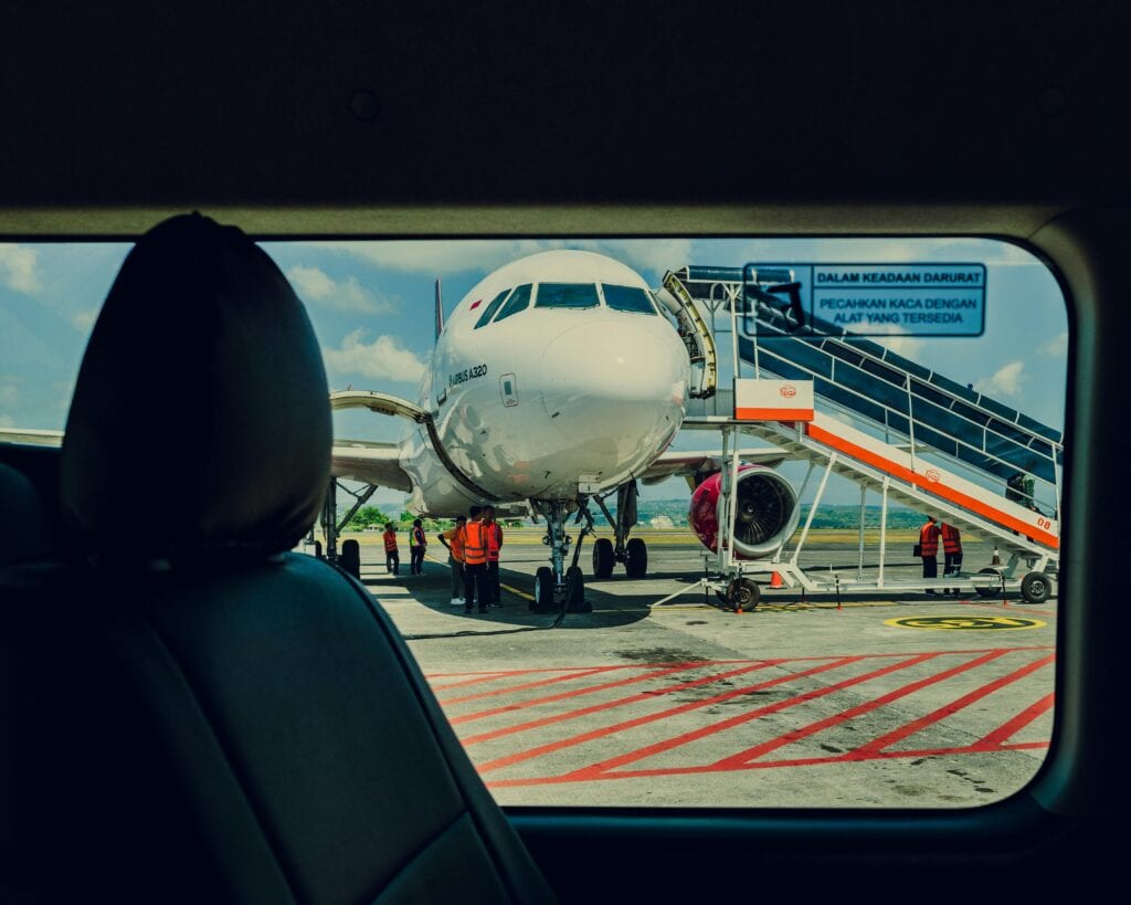 Airplane Viewed From A Car, Parked On The Tarmac At An Airport With Crew Working Nearby.