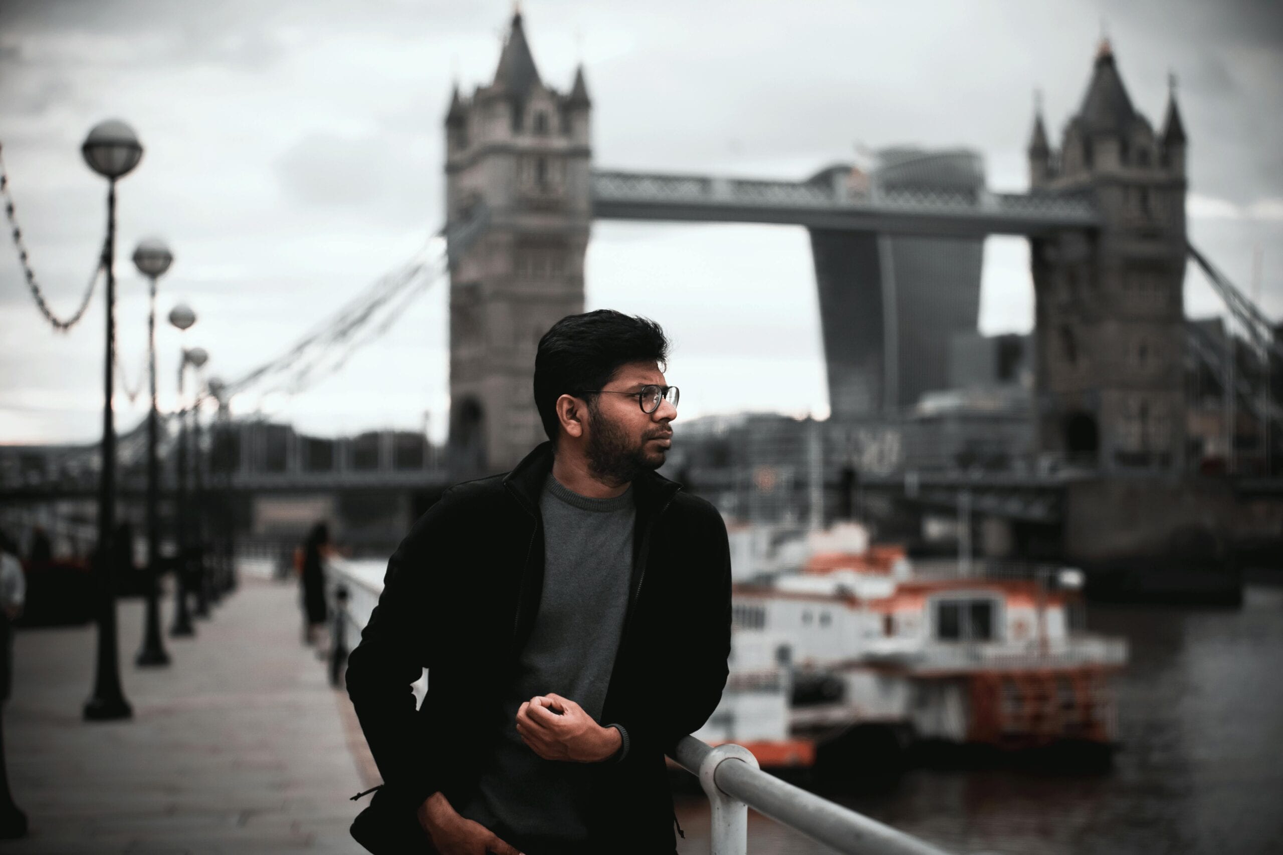 A Contemplative Man Poses With Tower Bridge And The Thames In The Background.
