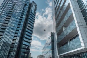 Modern Skyscrapers In Poznań With An Airplane Soaring Above On A Clear Day.