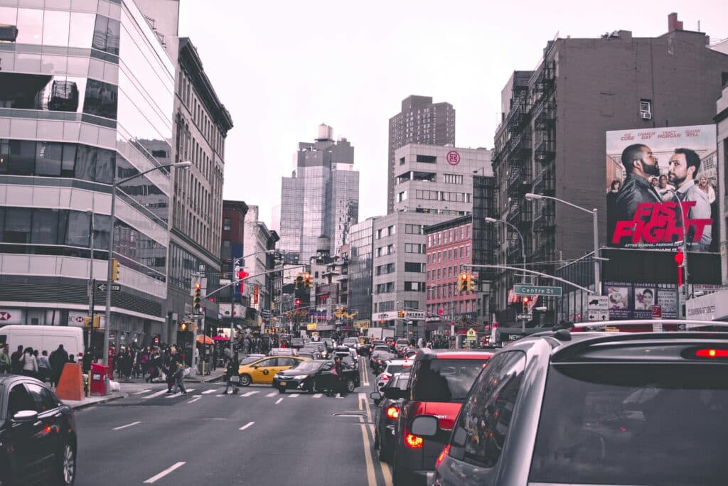 Lively City Street In New York With Bustling Traffic And Urban Buildings During The Day.
