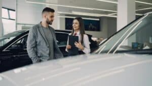 Man Consults With Salesperson In Modern Car Dealership Showroom.