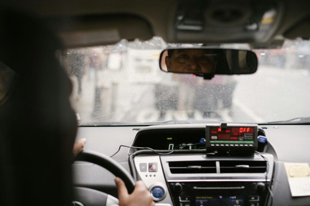 Back View Of Man Reflecting In Mirror While Driving Along Street In City On Urban Background In Soft Daylight