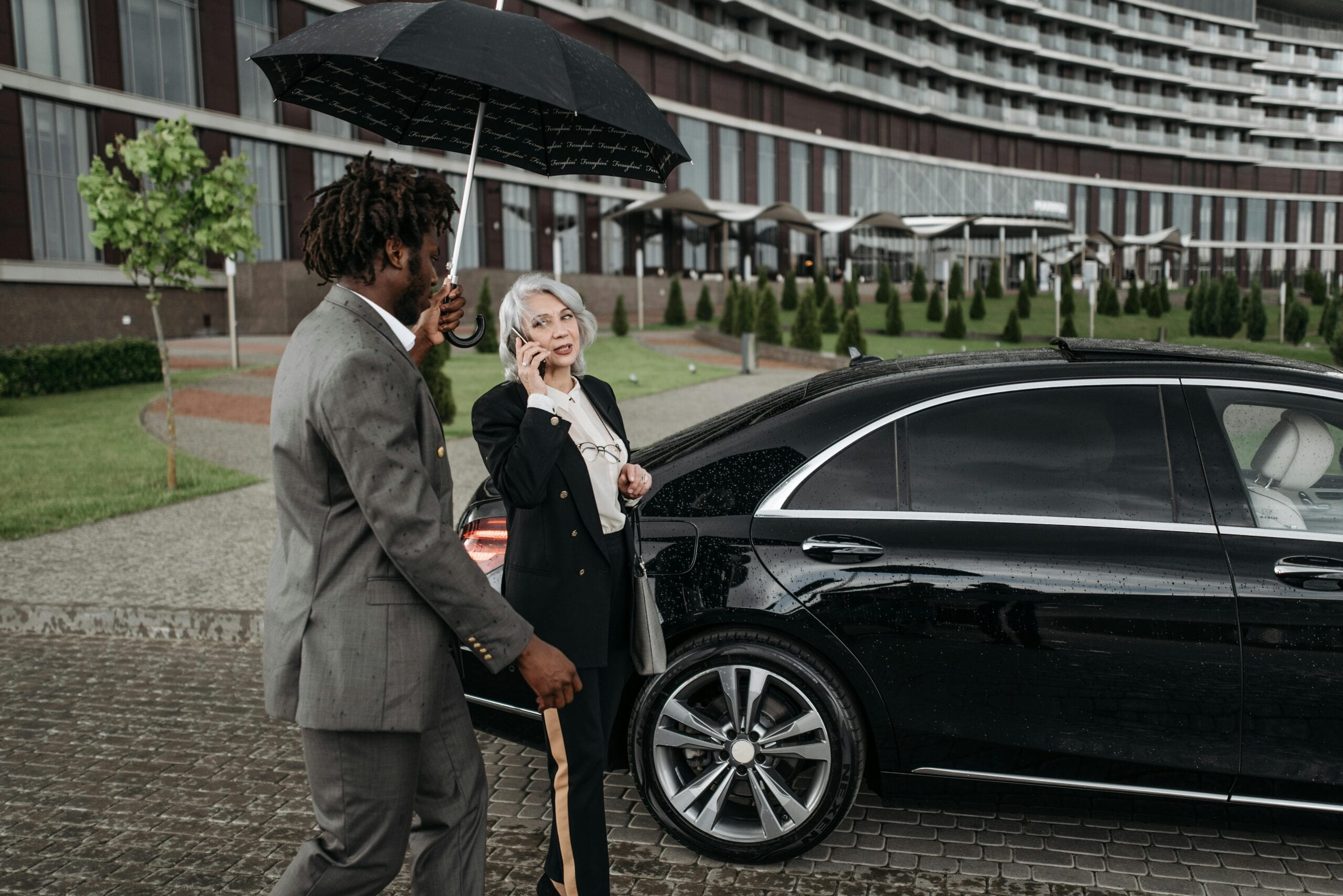 Blogs | Articles | News | Tips &Amp; Tricks | Video | Faq | Infomation 3 May 11, 2026 Two Business Professionals With A Luxury Car Outdoors, Using An Umbrella And Smartphone.