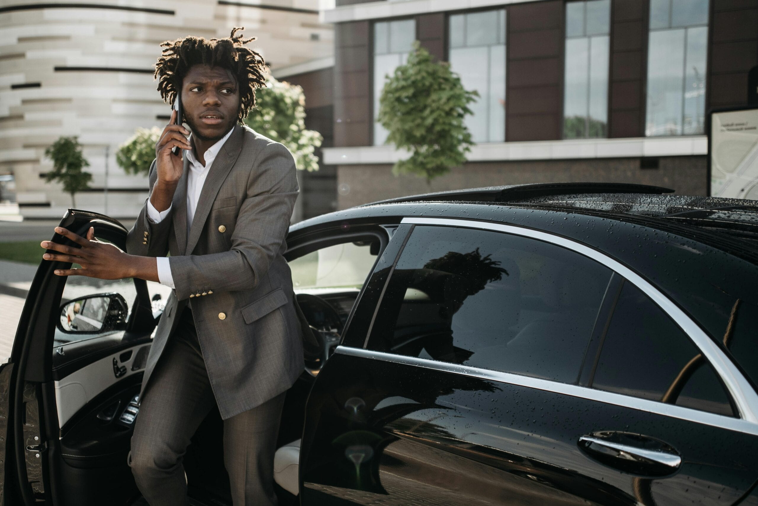 Confident Businessman In A Suit Talking On A Smartphone While Getting Out Of A Luxury Black Vehicle.