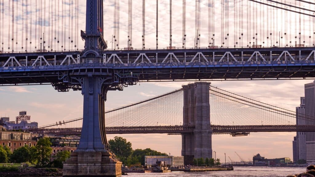 A Captivating View Of The Iconic Manhattan And Brooklyn Bridges Over The River At Sunset In New York City.