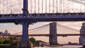 A Captivating View Of The Iconic Manhattan And Brooklyn Bridges Over The River At Sunset In New York City.