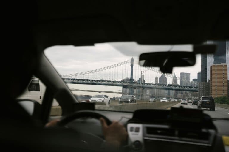 Back View Of Anonymous Male Driving Car Along Roadway Against Bridge On Urban Background In Soft Daylight