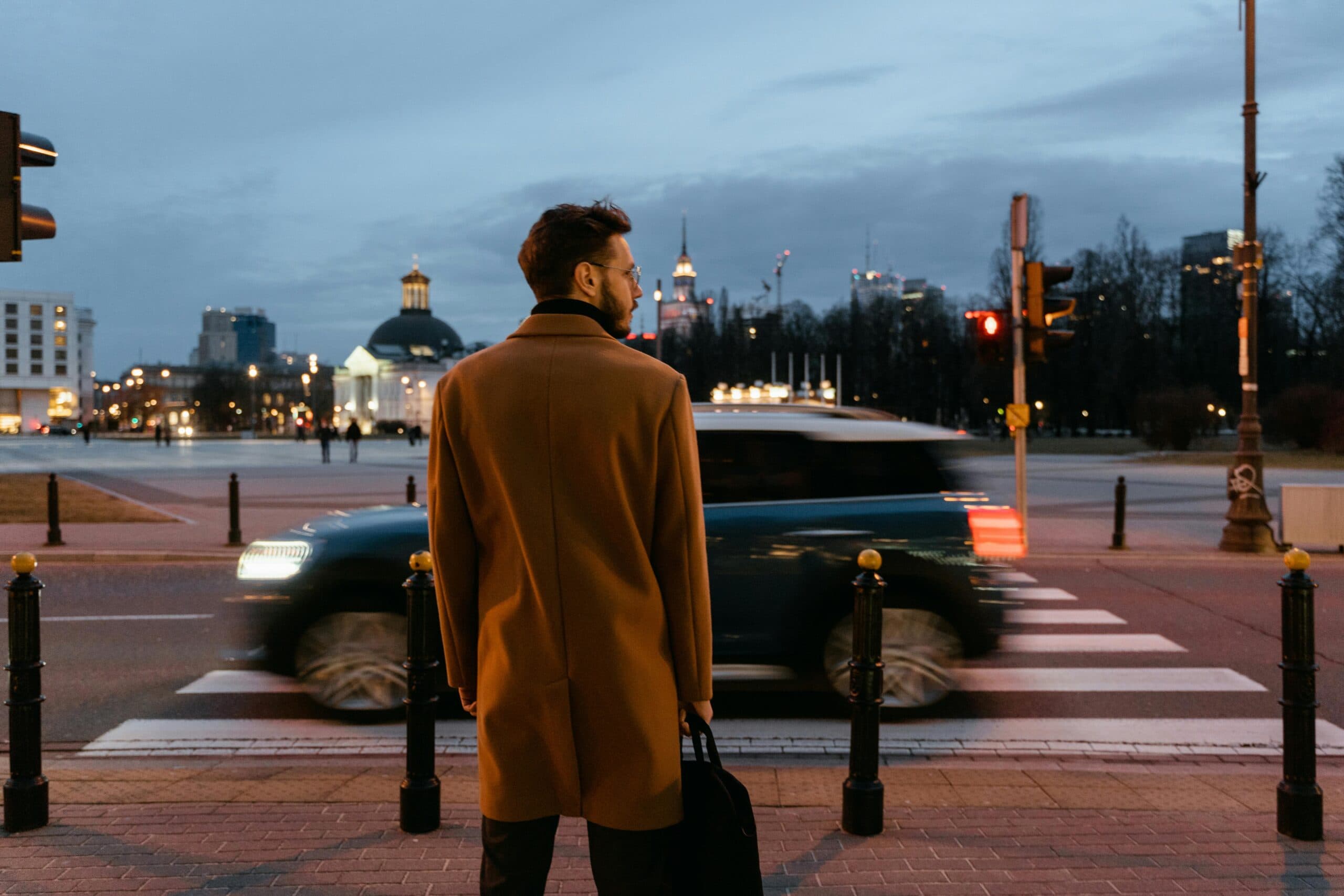 Blogs | Articles | News | Tips &Amp; Tricks | Video | Faq | Infomation 8 June 10, 2026 A Person Waiting At A Crosswalk In A City At Evening Twilight, With Blurred Car Lights Passing By.