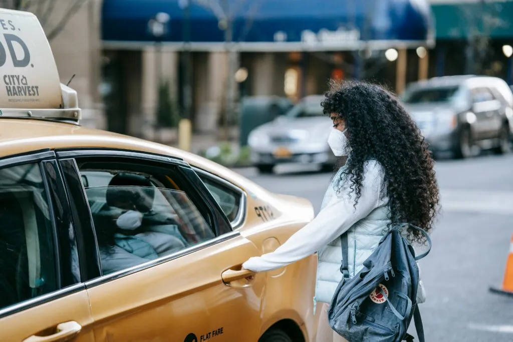 All About the best car rental NYC - Know Your Way Around This City Perfectly and Elegantly 2 Side view of unrecognizable African American lady with long dark hair in casual clothes and medical mask opening door of ta parked on city street