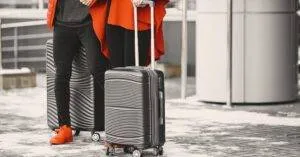 A Fashionable Couple In Winter Attire With Sleek Luggage, Standing Outdoors On A Snowy Day.