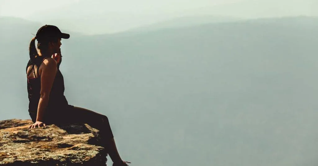 A Woman Enjoys A Calm Moment Sitting On A Cliff'S Edge Against A Foggy Mountainous Backdrop.