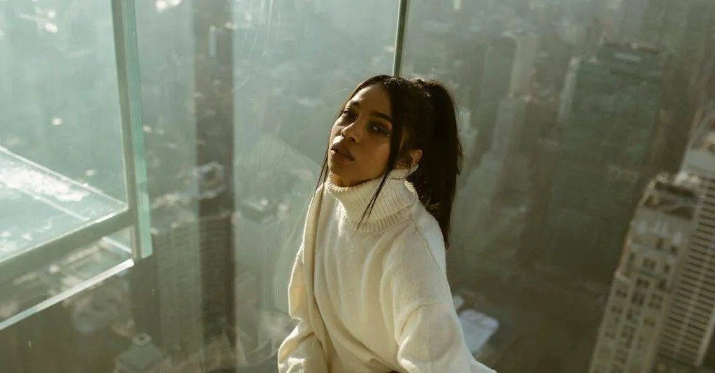 Young Woman In Cozy Sweater Posing By A Glass Wall Overlooking New York City From A Skyscraper.