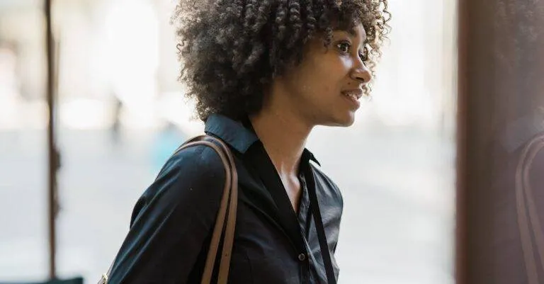 An Adult Woman With A Fashionable Afro Hairstyle Standing In An Urban Street Setting, Exuding Confidence.