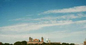 Scenic View Of Ellis Island As The American Flag Waves, Set Against A Clear Blue Sky.